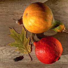 Different orange and yellow pumpkins lie on a wood textured background with an autumn leaf, acorn and cone, top view