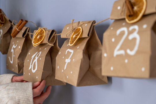 Advent calendar from craft paper with dry oranges and cinnamon on the wall with woman's hands.