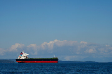 A large red and black cargo ship in mid harbor waiting to off load its cargo. 