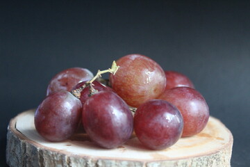some red grapes on a wooden placemat on a black background