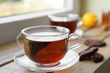 Bag of black tea in cups on wooden table indoors
