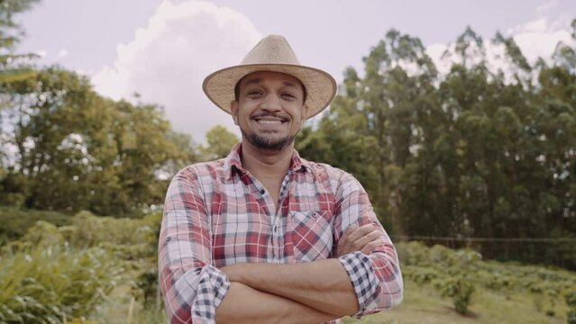 Portrait of young farmer man with crossing hands in the casual shirt and hat in the farm. Premium Cinematic 4K