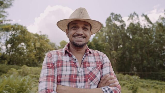 Portrait of young farmer man with crossing hands in the casual shirt and hat in the farm. Premium Cinematic 4K