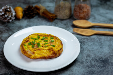 Breakfast yellow omelette with bacon topped with sliced spring onions on dark concrete close up view.