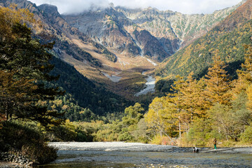Fototapeta premium Beautiful background of the center of Kamikochi national park by snow mountains, rocks, and Azusa rivers from hills covered with leaf change color during the Fall Foliage season.