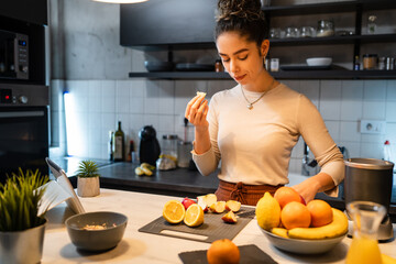 One woman young adult happy caucasian female smile while cutting and eating fruit at the kitchen counter in the morning healthy eating vegan and vegetarian concept real people copy space