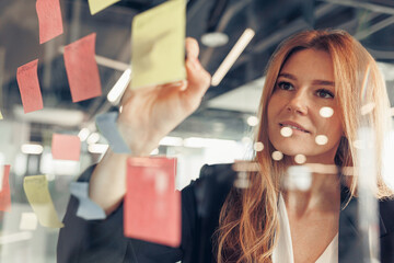 Businesswoman writing on sticky notes on glass wall while working in office