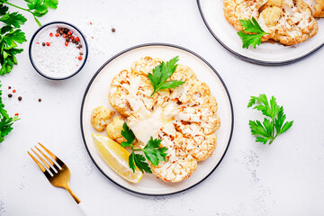Baked cauliflower steak on plate, white table background, top view