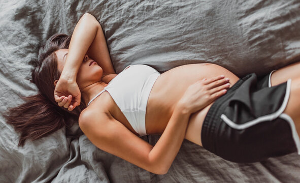 Tired pregnant woman sleeping on bed hiding face crying in depression or feeling morning sickness nausea. Could be used for Mental health, fatigue, stress and depression during pregnacy