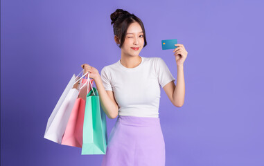 Young Asian woman holding shopping bag on purple background