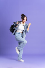 Portrait of a beautiful Asian schoolgirl wearing a backpack on a purple background
