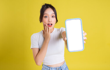 Young Asian woman holding phone with cheerful face on yellow background - obrazy, fototapety, plakaty