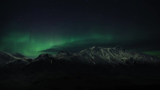 Northern Lights (Aurora Borealis) on the night sky above the snowy mountain range. Time Lapse. 