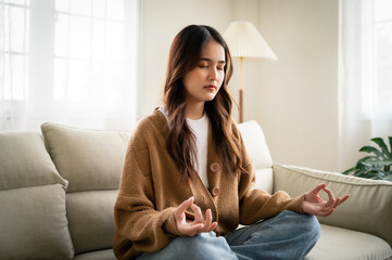 Young asian woman hand meditating and sitting on couch in living room at house