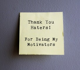 Yellow Note on grey wall with text THANK YOU HATERS , FOR BEING MY MOTIVATORS - Self reminder to...