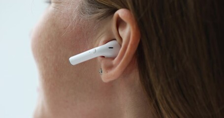 Young woman putting wireless earphone into ear close up. Gadget user lady showing using white small earbud for listening to music, video phone call. Cropped shot - Powered by Adobe