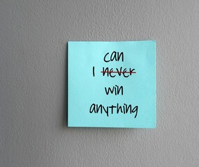Blue note on gray wall written I NEVER WIN ANYTHING (red cross on NEVER and replace with CAN) concept of change nagative self talk to positive one, overcoming inner voice critic