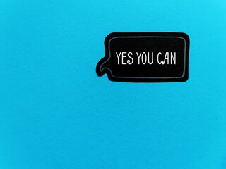 Black sticker on blue copy space background with text YES YOU CAN, concept of self talk or...