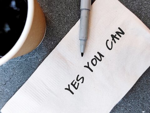 Coffee cup and pen on paper napkin with text written YES YOU CAN, concept of self talk or affirmation, to support oneself that everything is possible if you set goal and never give up to achieve it