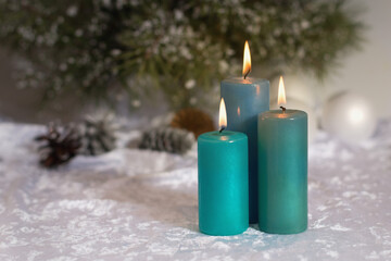 Burning green, blue candles and cones on the background of a fir tree in a Christmas composition. Place for recording. Close-up.