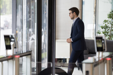 Millennial businessman in formal suit leaving office building area, passes through doorway,...