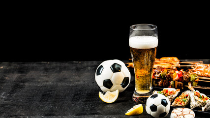 A variety of barbecue dishes and beer are placed on the black wooden background.Watch football and eat barbecue