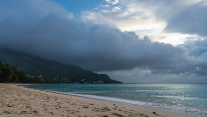 Fototapeta na wymiar A calm foggy day on a tropical beach. The foam of the waves of the turquoise ocean on the sand. The top of the hill is hidden in clouds. Seychelles. Mahe. Beau Vallon