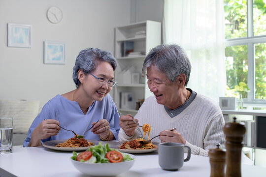 Happy Asian Senior Couple Eating Meal Together In Kitchen At Home. Retirement Senior Couple Lifestyle Living Concept.