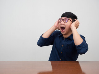 Young businessman wear glasses sit at the desk hold his head feels amazed