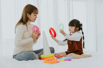Mom and little 4 years old kid daughter playing education colourful ring toy together at living room