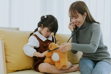 Young asian mother and kid girl daughter with stethoscope sitting on couch role play doctor with...