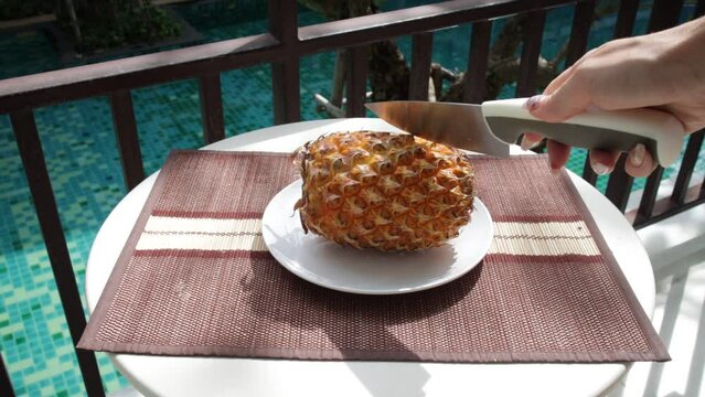 A girl's hand cuts a pineapple