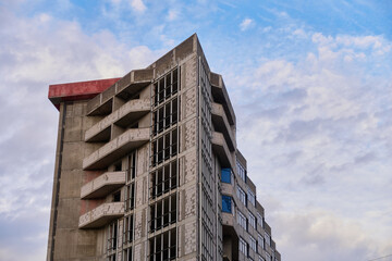 An apartment building under construction made of brick and monolith. Concrete structure with balconies and window openings. Blue cloudy sky.