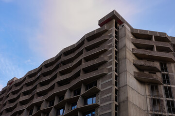 An apartment building under construction made of brick and monolith. Concrete structure with balconies and some glazed window openings. Blue cloudy sky.