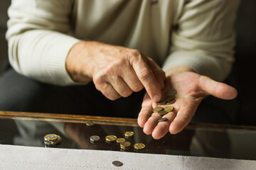 Senior man counting coins on table in a period of crisis. Old man holds handful of poland coins and calculating money.