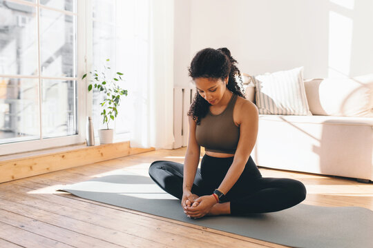 Active african american pregnant woman practicing yoga, sitting in butterfly or konasana pose, stretching muscles on mat, doing prenatal exercises for healthy pregnancy and prepare body for childbirth