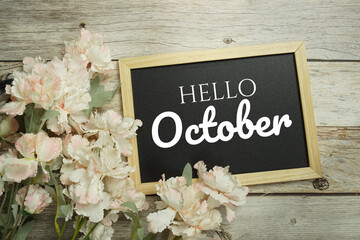 Hello October text message on blackboard with flower decoration on wooden background
