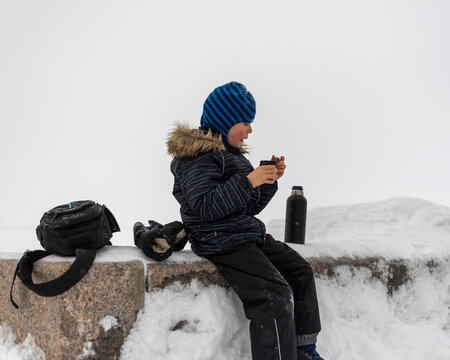 a boy in the fresh winter air after a walk drinks hot tea from a thermos with a chocolate bar. the concept of rest in winter