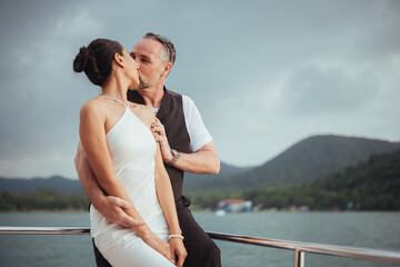 Romantic couple love hugging and kissing on yacht. Happy man and woman standing and hugging in cruise ship while sunset on vacation. luxury and honeymoon lifestyle, Happy aniversary.