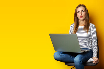 Naklejka premium Young woman sitting on chair and holding laptop on isolated yellow background.