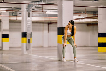 A sportswoman is leaning on pillar and taking a break after exercises.