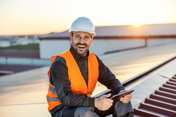 Portrait of happy worker with tablet checking on solar panels on the roof.