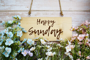 Happy Sunday text message with flowers on wooden background