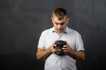 a man of European appearance holds a black skull in his hands. teacher. place for text