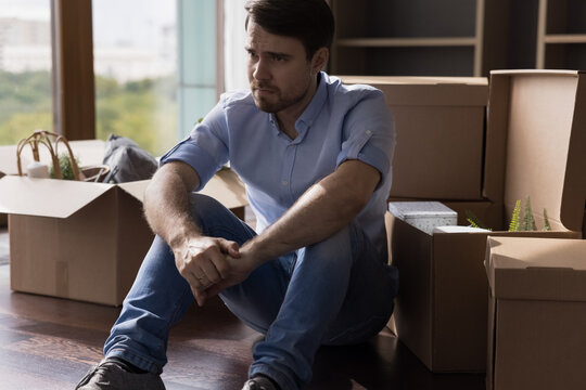 Depressed man moves out from flat, sit near heap of carton boxes with personal stuff, deep in sad thoughts, think over financial problems, job loss, bankruptcy, eviction, bank take house due loan debt