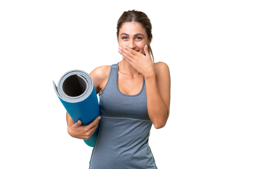 Pretty Young Uruguayan sport woman going to yoga classes while holding a mat over isolated background happy and smiling covering mouth with hand