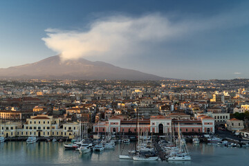 Port of Catania. Volcano Etna with white smoke and blue sky on background. Sicily, Italy