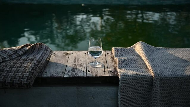 A glass of wine stands by the pool at sunset. There is a blanket next to it. Cozy autumn day