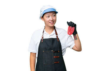 Young caucasian woman wearing an apron and serving fresh cut meat over isolated background looking to the side and smiling