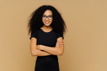Slim satisfied woman with Afro haircut, wears black casual clothes, optical glasses, has confident...